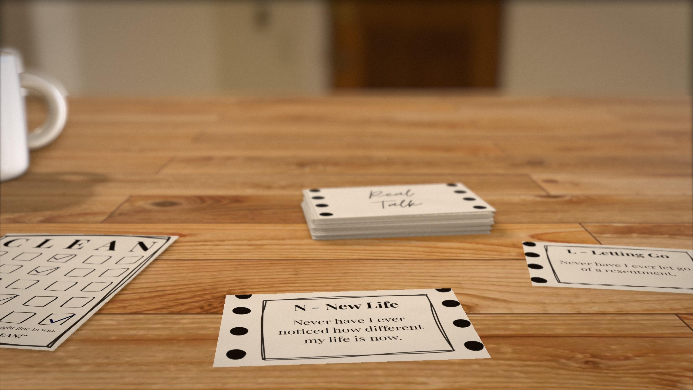 CLEAN recovery game on a wooden table, with a stack of Real Talk cards, face-up prompt cards and a CLEAN bingo board marked with pen checks